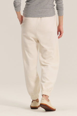 A person in Velvet by Graham & Spencer's DAWN JOGGER off-white sherpa fleece pants with a relaxed fit, paired with a grey long-sleeve top and beige shoes, stands facing away from the camera.