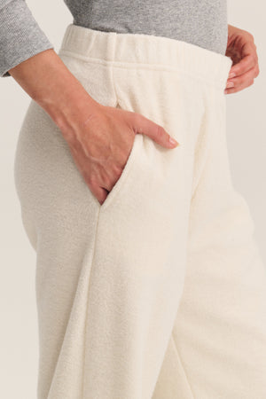 A person wearing the DAWN JOGGER by Velvet by Graham & Spencer in cream sherpa fleece, hand in pocket, paired with a light gray long-sleeve top for a cozy, relaxed silhouette.
