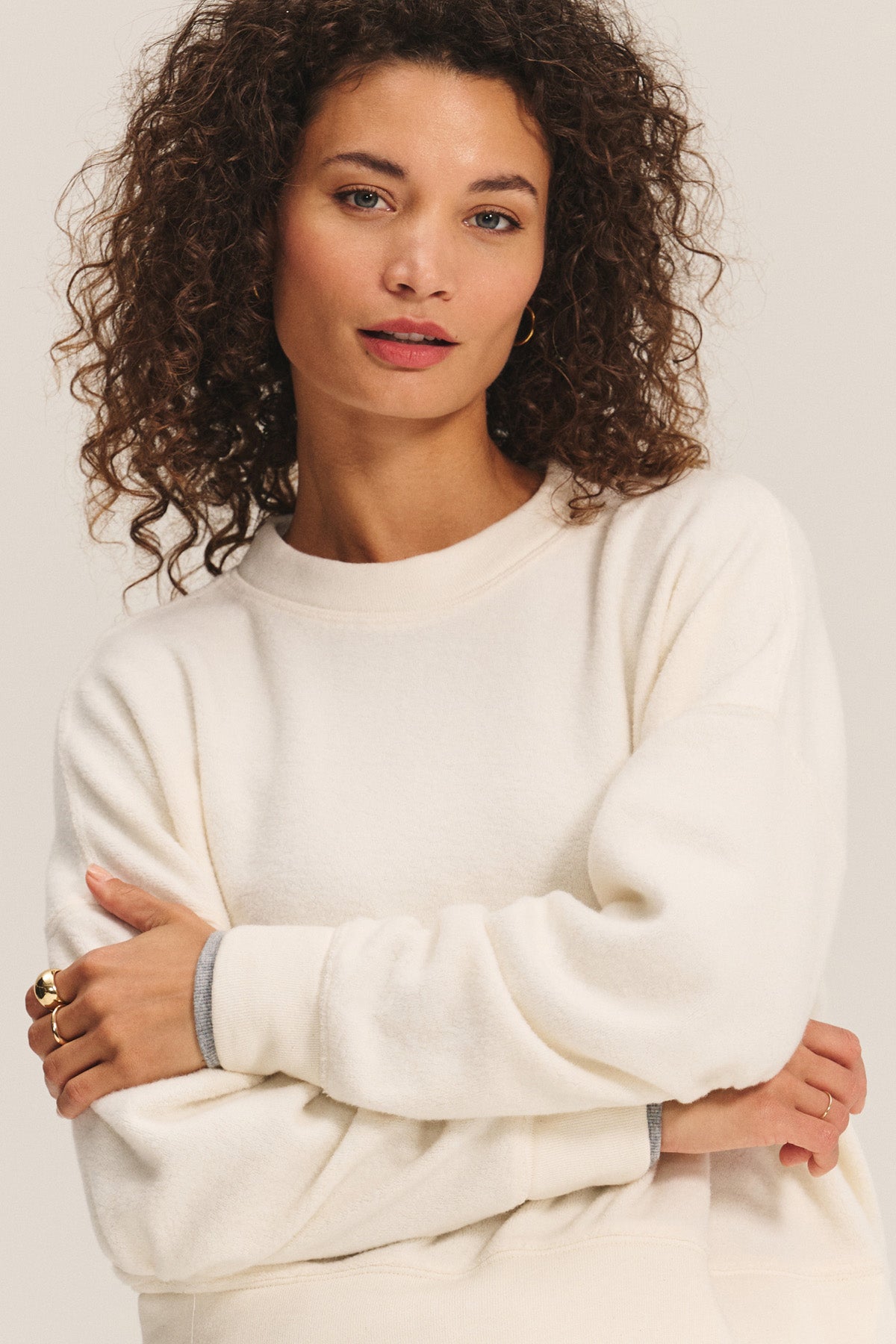 A woman with curly hair wears the ultra-soft KIMMY SWEATSHIRT by Velvet by Graham & Spencer, standing with arms crossed and looking at the camera against a plain background.-40461667172545