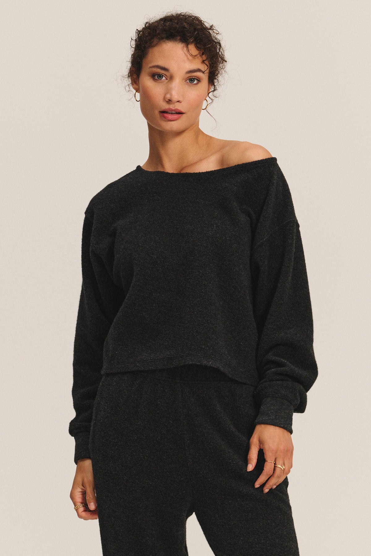 A woman stands facing the camera against a plain background, wearing the Velvet by Graham & Spencer MALLORY SWEATSHIRT and matching black pants.