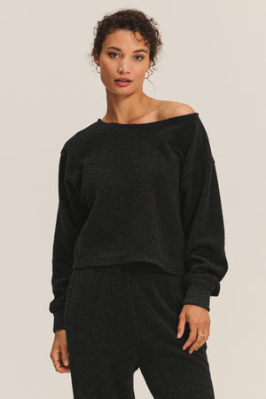 A woman stands facing the camera against a plain background, wearing the Velvet by Graham & Spencer MALLORY SWEATSHIRT and matching black pants.