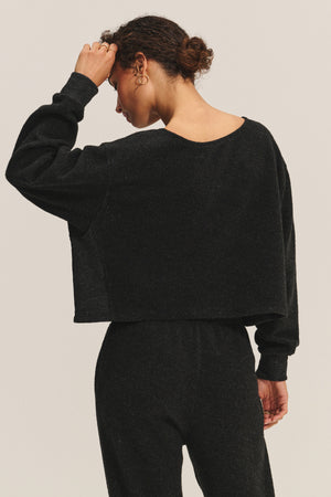 A person is shown from the back, wearing the cozy black MALLORY SWEATSHIRT by Velvet by Graham & Spencer and matching pants, with one hand touching their head.