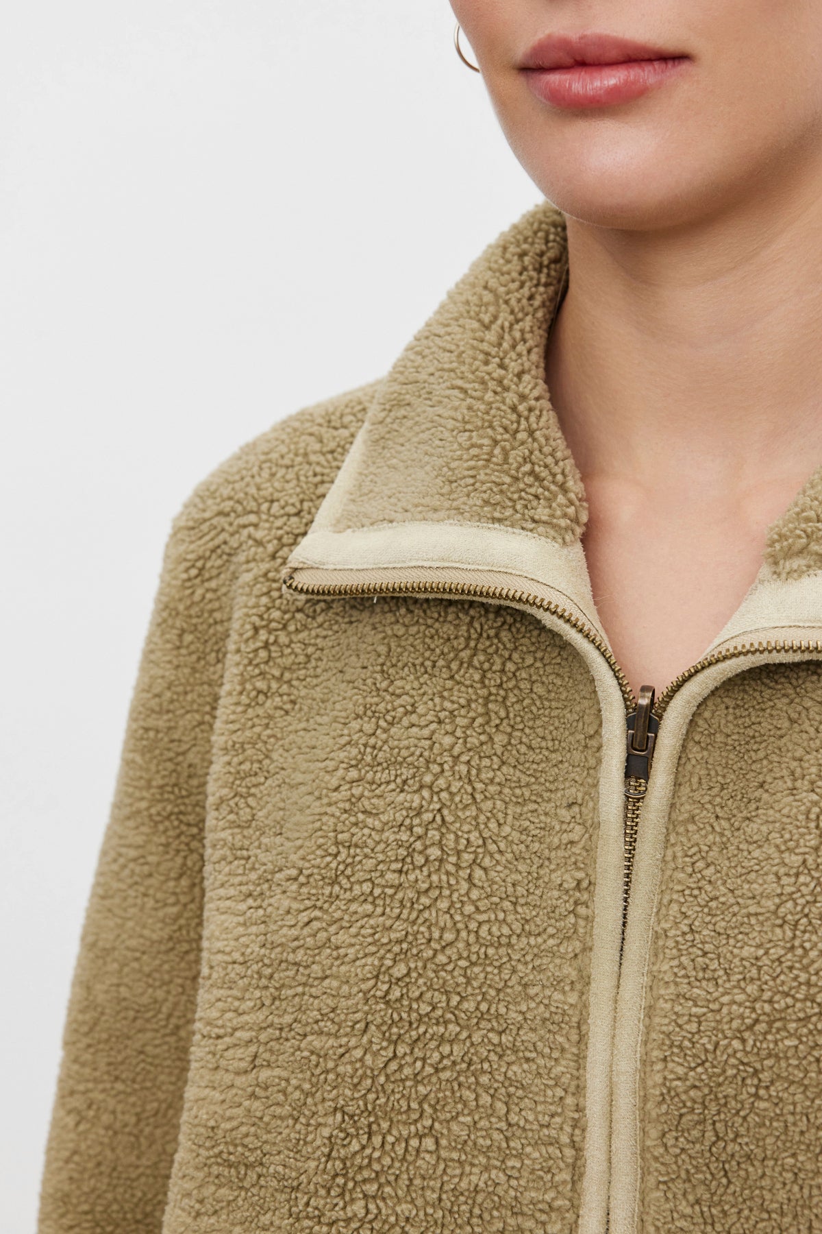   A person wearing the REBA REVERSIBLE SHERPA JACKET from Velvet by Graham & Spencer gives off a cozy feel, especially with its beige, fuzzy faux sherpa design emphasizing the upper part of the body. 