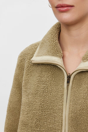 A person wearing the REBA REVERSIBLE SHERPA JACKET from Velvet by Graham & Spencer gives off a cozy feel, especially with its beige, fuzzy faux sherpa design emphasizing the upper part of the body.