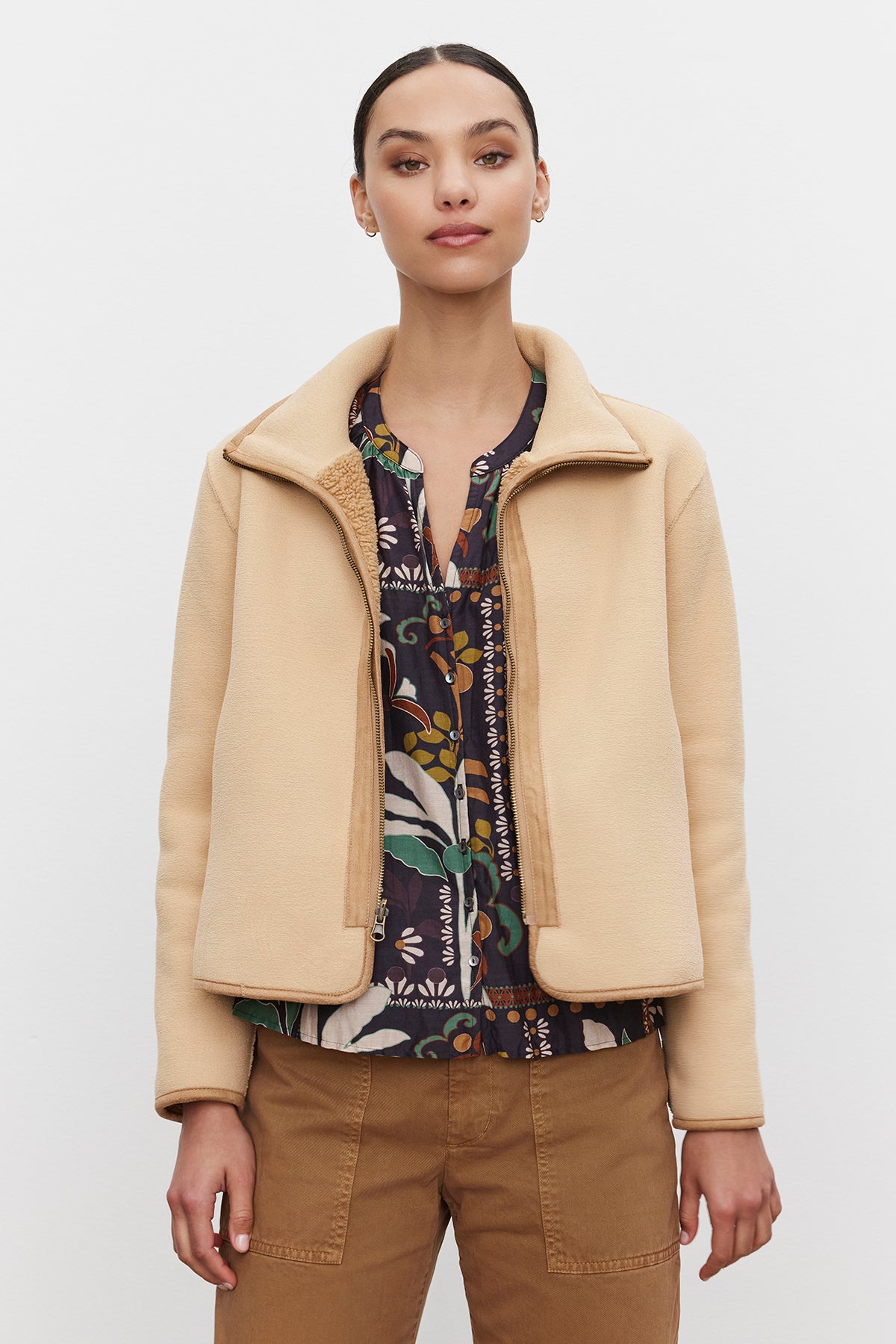   A person stands wearing the REBA REVERSIBLE SHERPA JACKET from Velvet by Graham & Spencer over a patterned shirt and brown pants, posing against a plain white background. 