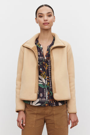 A person stands wearing the REBA REVERSIBLE SHERPA JACKET from Velvet by Graham & Spencer over a patterned shirt and brown pants, posing against a plain white background.