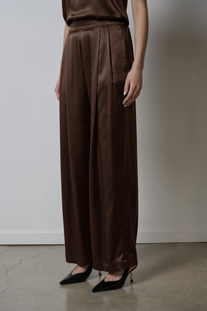 The model is wearing a brown silk jumpsuit with wider leg pants in Velvet by Jenny Graham's MANHATTAN PANT.