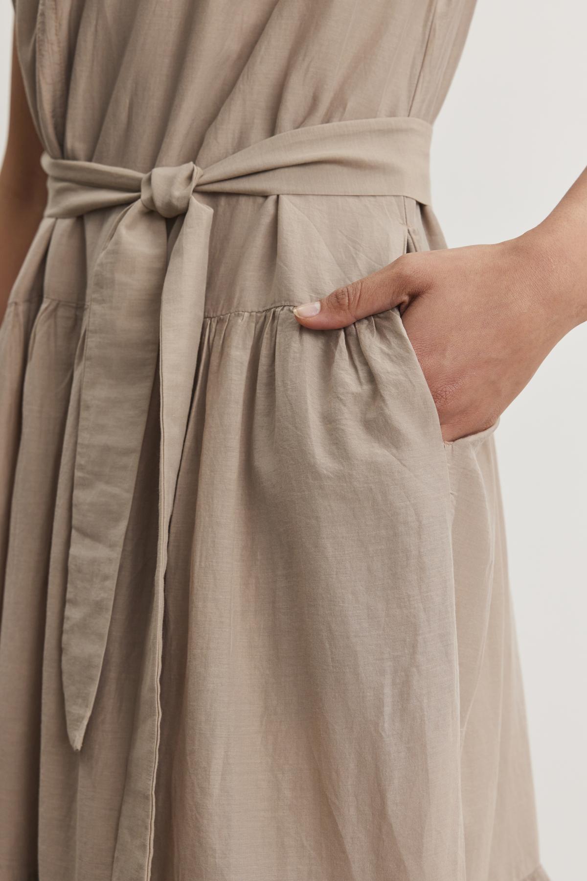   Close-up of a person wearing the ADA SILK COTTON VOILE DRESS by Velvet by Graham & Spencer, showcasing its tied waist belt and a hand placed in the dress pocket. 