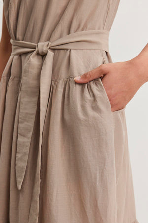 Close-up of a person wearing the ADA SILK COTTON VOILE DRESS by Velvet by Graham & Spencer, showcasing its tied waist belt and a hand placed in the dress pocket.