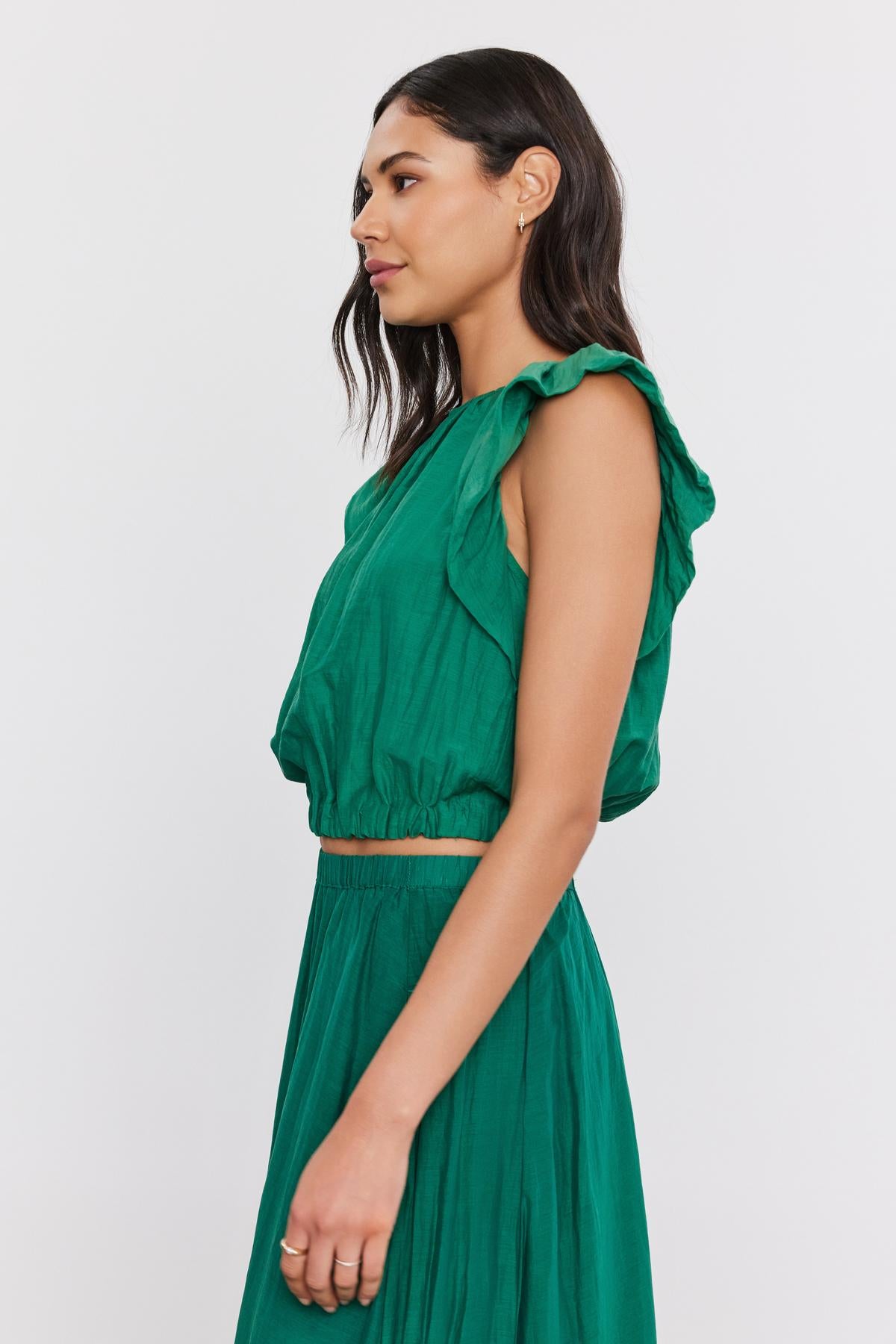   Profile view of a woman in a green ruffled Amora Top by Velvet by Graham & Spencer, with a crew neckline, looking to the side against a white background. 