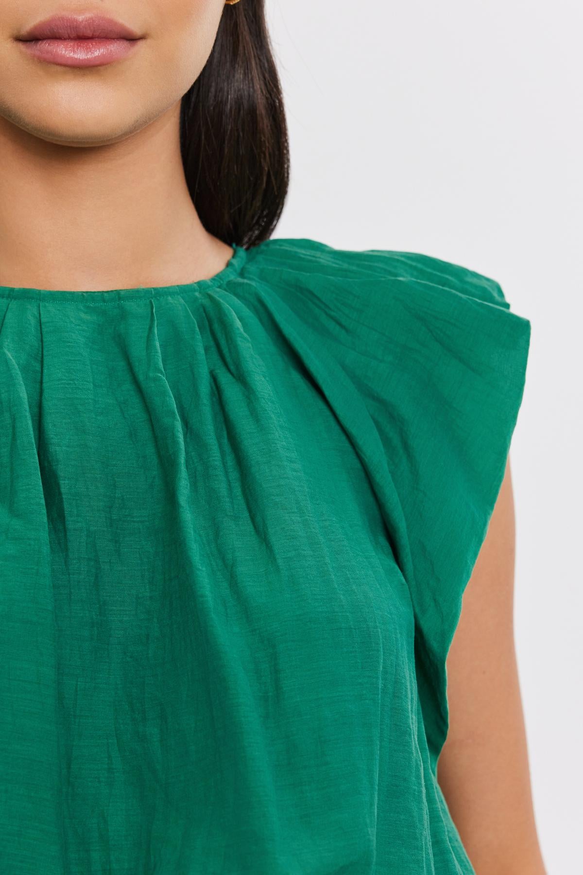   Close-up of a woman wearing a green silk cotton voile AMORA TOP by Velvet by Graham & Spencer with gathered detailing at the shoulder. Only the lower half of her face and shoulder are visible. 