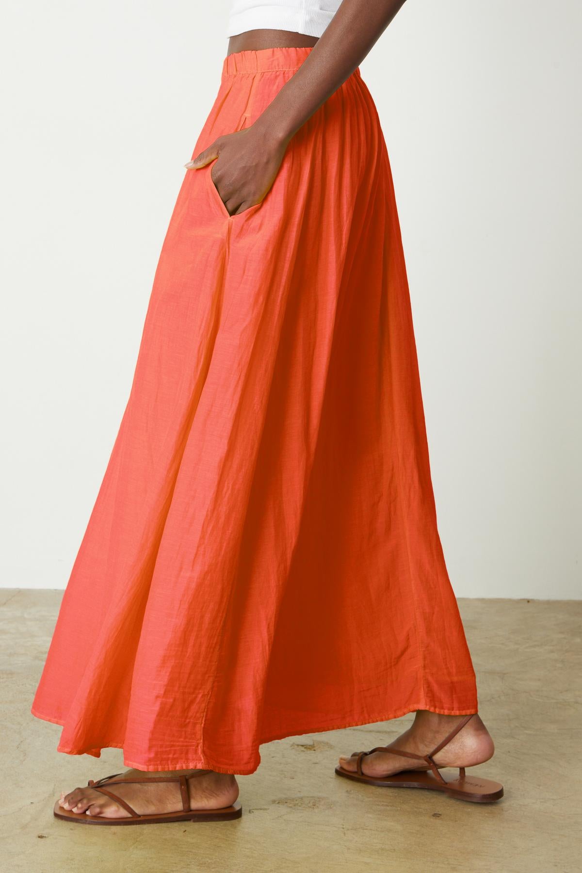   A person wearing the MARIELA SKIRT by Velvet by Graham & Spencer, a long, orange silk cotton voile skirt with hidden pockets. 