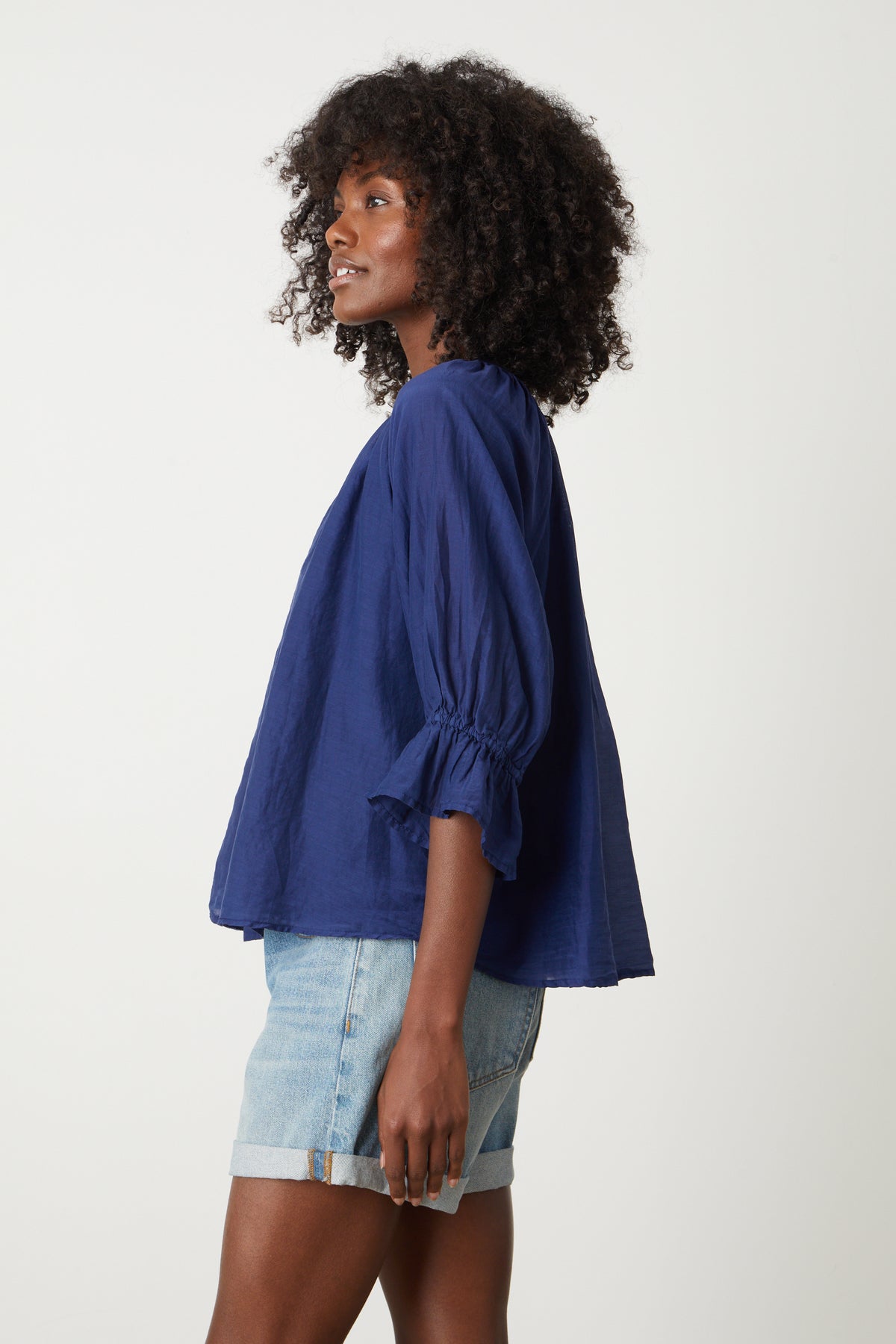 The model is wearing a blue Velvet by Graham & Spencer MARINA RUFFLE SLEEVE V-NECK BLOUSE.-26757632032961