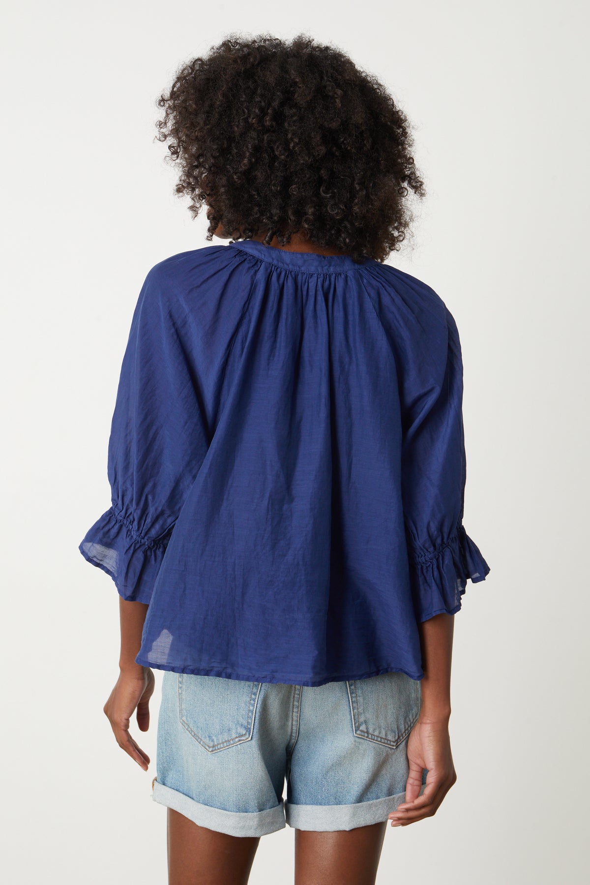   The back view of a woman wearing a Velvet by Graham & Spencer MARINA RUFFLE SLEEVE V-NECK BLOUSE with ruffled sleeves. 