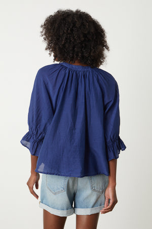 The back view of a woman wearing a Velvet by Graham & Spencer MARINA RUFFLE SLEEVE V-NECK BLOUSE with ruffled sleeves.