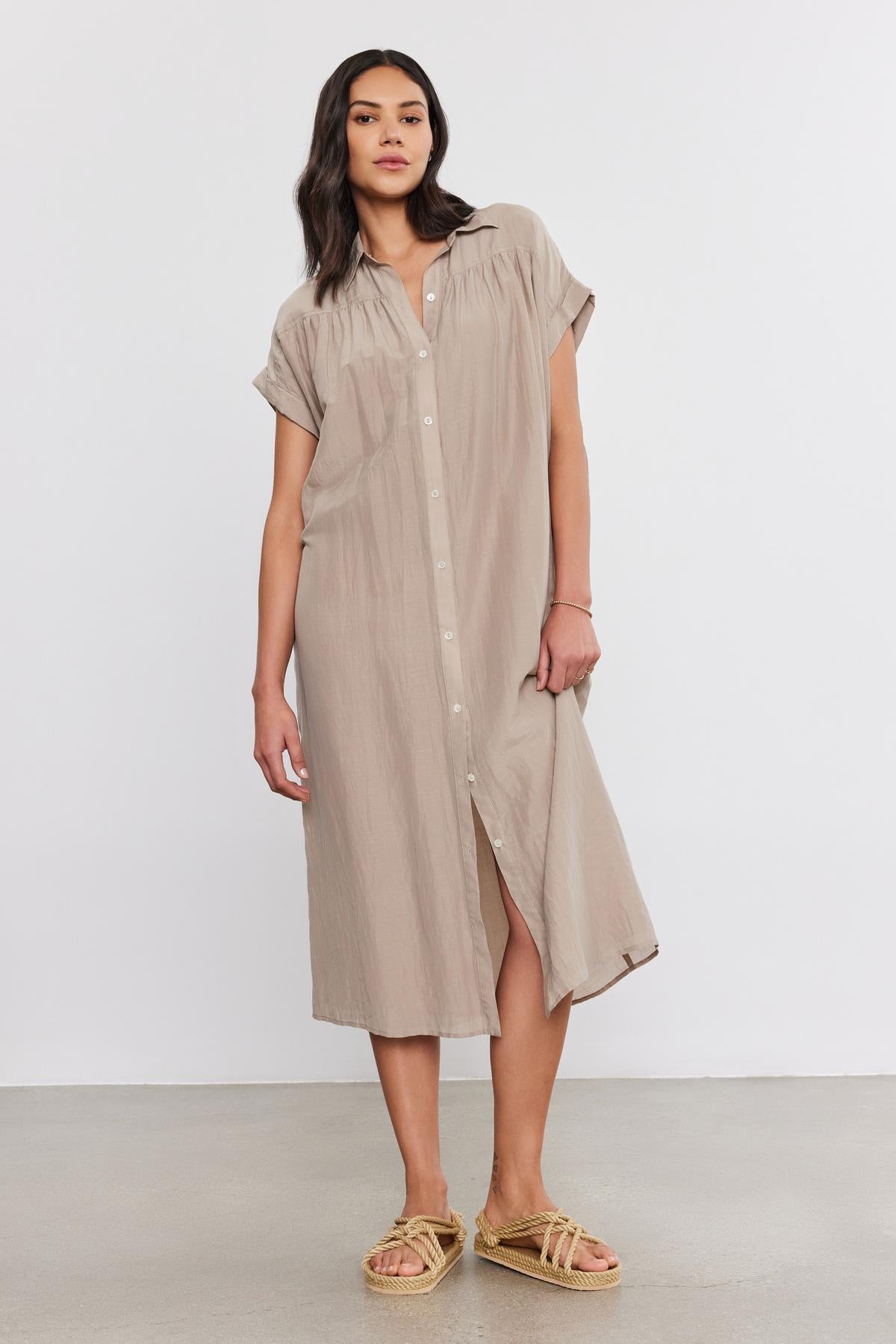   A woman with long dark hair wears the MARLA SILK COTTON VOILE DRESS by Velvet by Graham & Spencer and beige sandals, standing against a plain white background. 