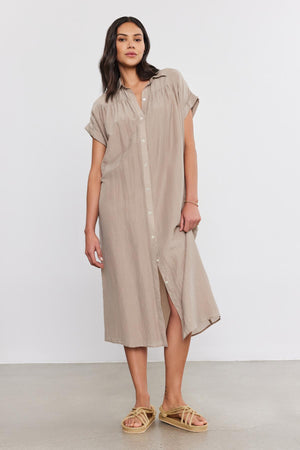 A woman with long dark hair wears the MARLA SILK COTTON VOILE DRESS by Velvet by Graham & Spencer and beige sandals, standing against a plain white background.