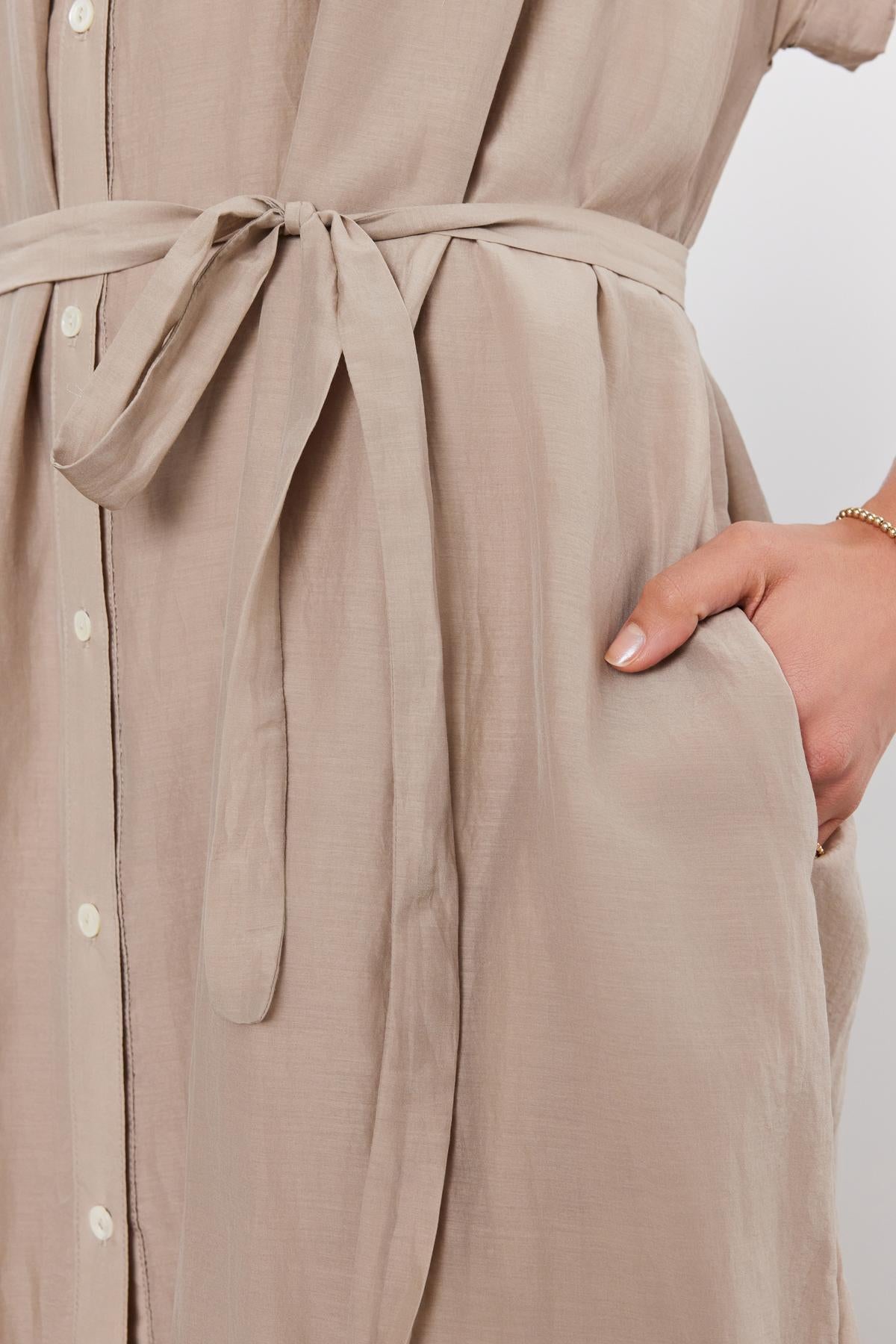   Close-up of the MARLA SILK COTTON VOILE DRESS by Velvet by Graham & Spencer, featuring buttons down the front, a tied belt at the waist, and a person’s hand in the side pocket. 