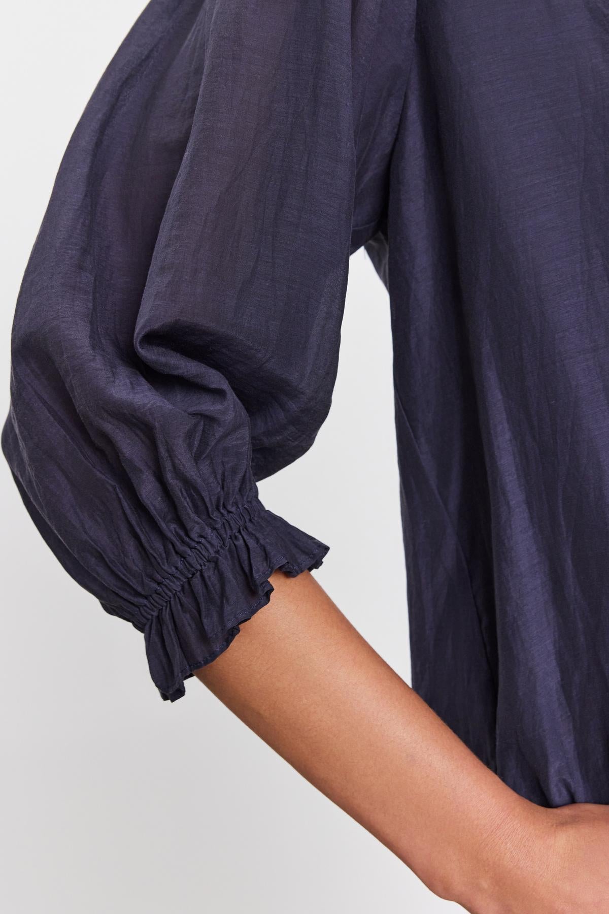   Close-up image of a person's arm and shoulder wearing the MEL SILK COTTON VOILE BUTTON-UP TOP by Velvet by Graham & Spencer. The sleeve is gathered at the cuff with elastic, creating a ruffled appearance. 