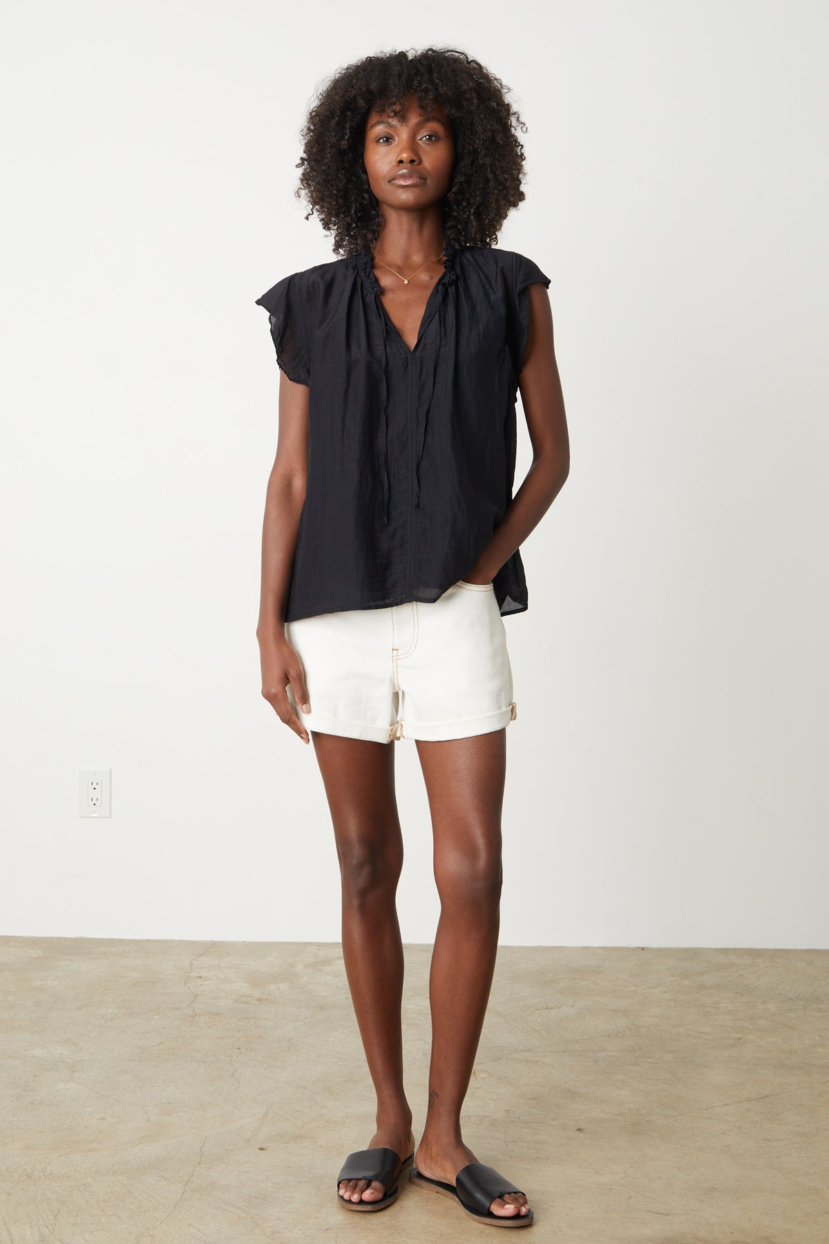 The model is wearing a Velvet by Graham & Spencer white silk MELANIE V-NECK BLOUSE and shorts in a display of lightness and romance.-35205235704001