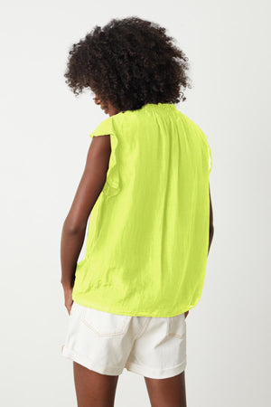 the back view of a woman wearing a MELANIE V-NECK BLOUSE by Velvet by Graham & Spencer and white shorts.
