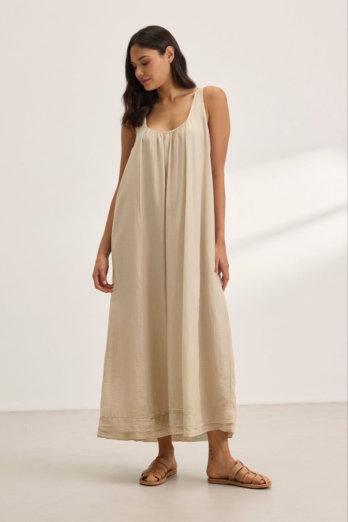 A woman stands in a minimalistic setting wearing the BAYOU SILK COTTON VOILE DRESS by Velvet by Graham & Spencer with sandals, highlighting versatile styling.-38801131307201