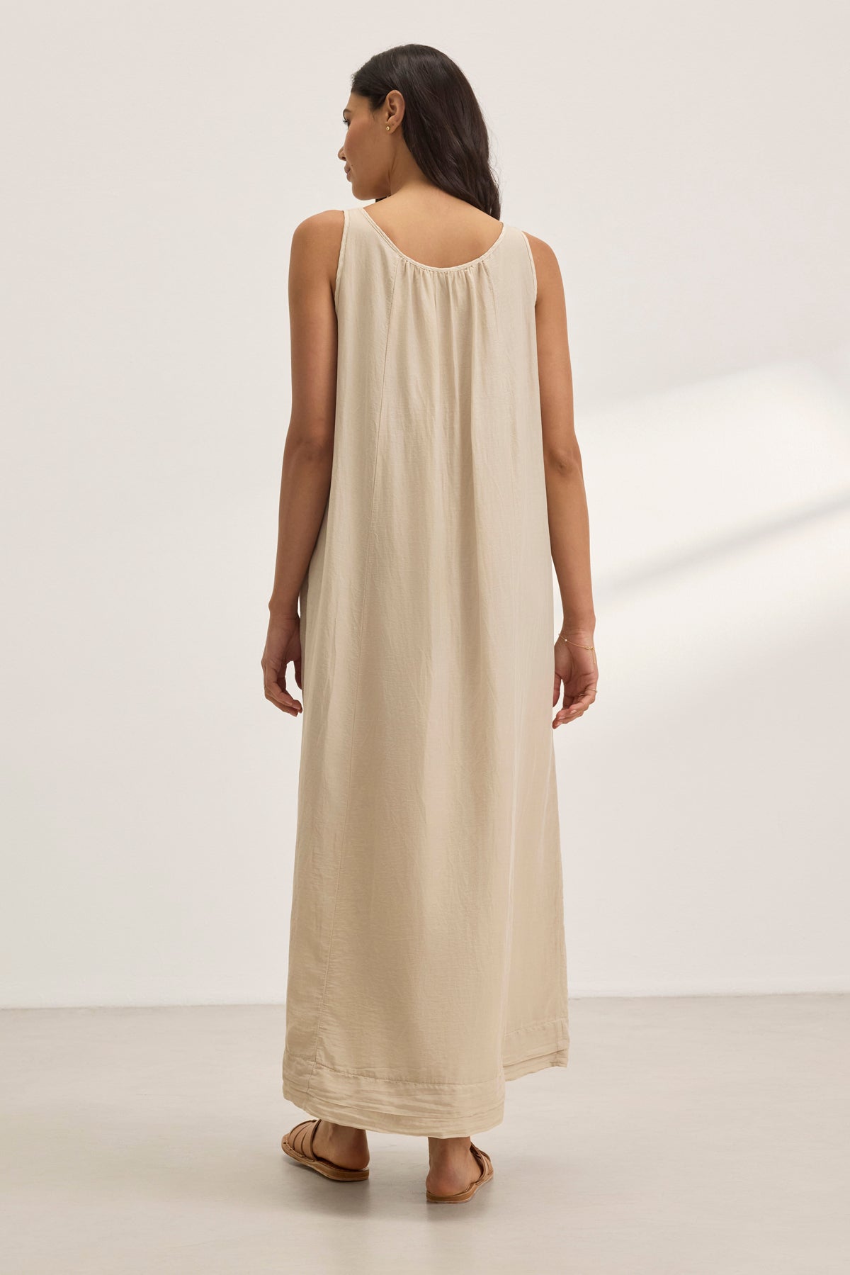 Someone in the BAYOU SILK COTTON VOILE DRESS by Velvet by Graham & Spencer, a sleeveless floor-length beige dress, stands on a light-colored floor facing away. The silk cotton voile fabric adds elegance for versatile styling in any setting.-38801131241665