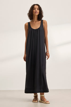 A woman wears the BAYOU SILK COTTON VOILE DRESS by Velvet by Graham & Spencer—a sleeveless, loose-fit maxi with a detachable belt—paired with light sandals, standing indoors against a plain background.