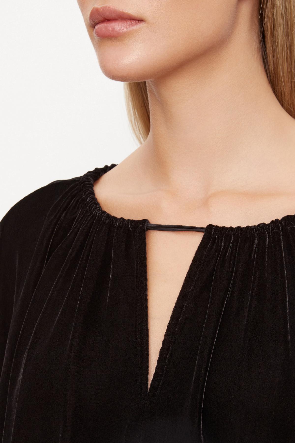   A woman wearing a NOA SILK VELVET CROPPED TOP by Velvet by Graham & Spencer, with an adjustable tie and pleated neckline. 