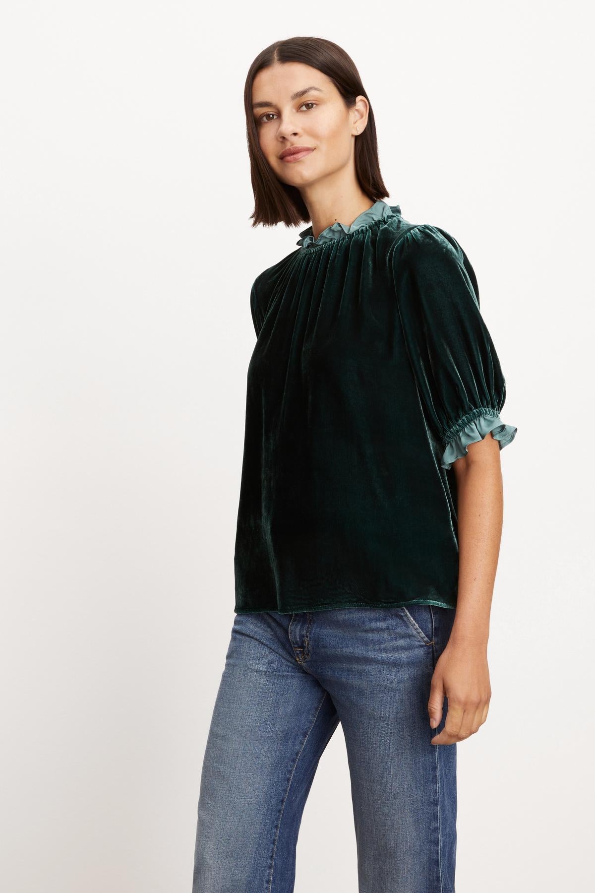 The model is wearing a green VAL SILK VELVET TOP with ruffles from Velvet by Graham & Spencer.-35654473187521