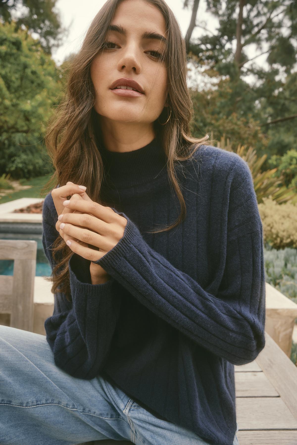 A woman in a cozy SIMONE CASHMERE MOCK NECK SWEATER from Velvet by Graham & Spencer sits outdoors, surrounded by trees, wearing jeans.-38483649069249