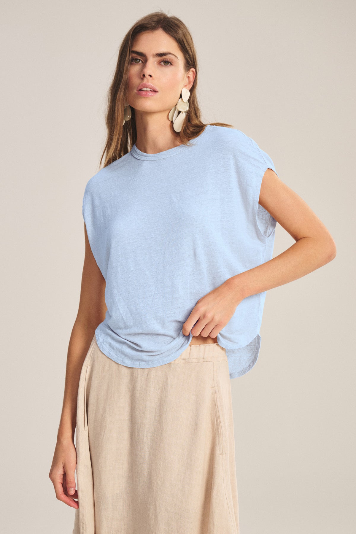 A woman stands against a neutral background wearing the Velvet by Graham & Spencer SINCLAIR TEE, styled with a beige skirt and drop earrings, effortlessly showcasing its breathable comfort.-41008439427265