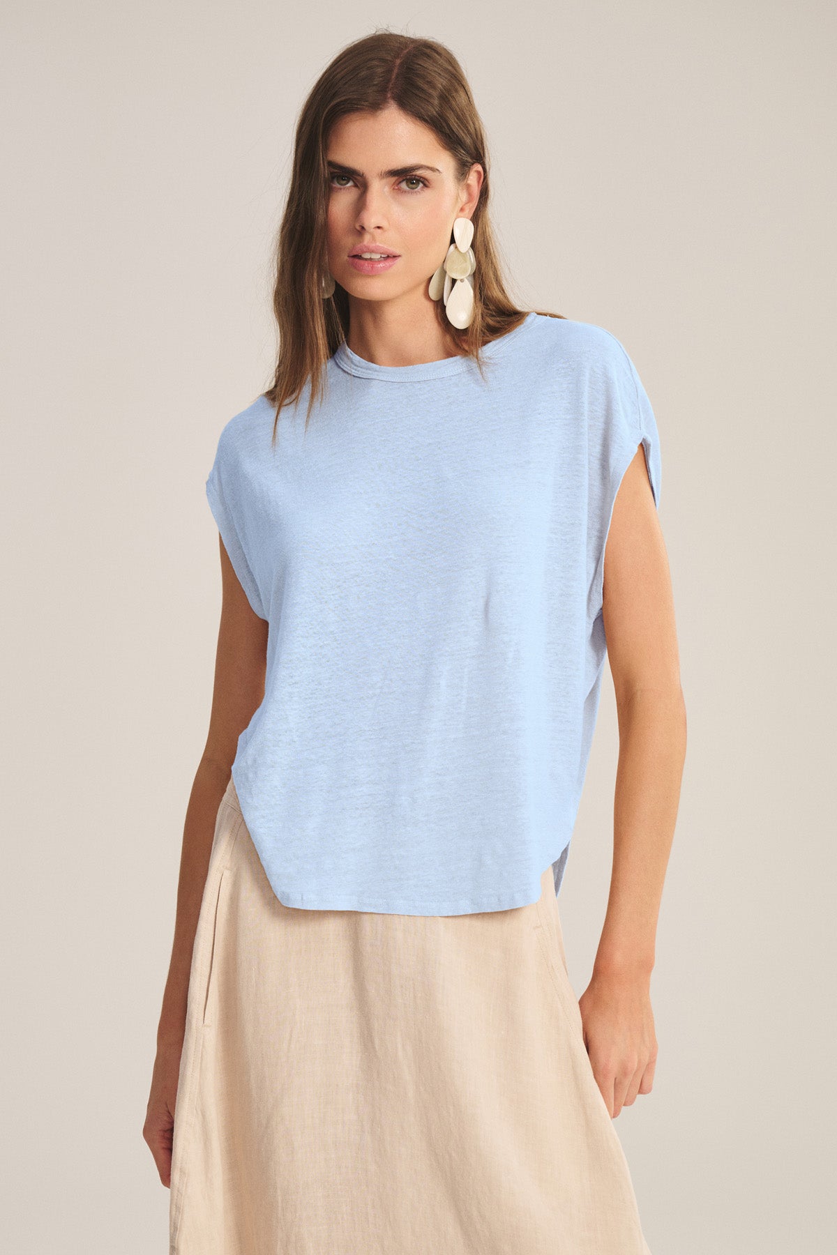 A woman wears the SINCLAIR TEE by Velvet by Graham & Spencer, a light blue linen knit sleeveless top, paired with a beige skirt and standing against a neutral background, exuding breathable comfort.-41008439460033