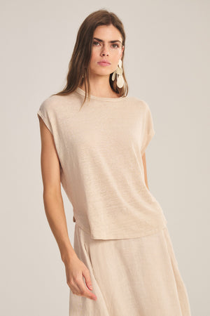 Woman wears the SINCLAIR TEE by Velvet by Graham & Spencer, a matching linen knit sleeveless top and beige cocoon silhouette skirt, standing against a plain background and looking at the camera.