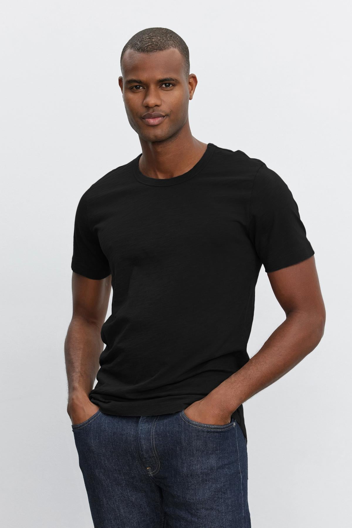   A man wearing a black AMARO CREW NECK SLUB TEE by Velvet by Graham & Spencer and jeans. 