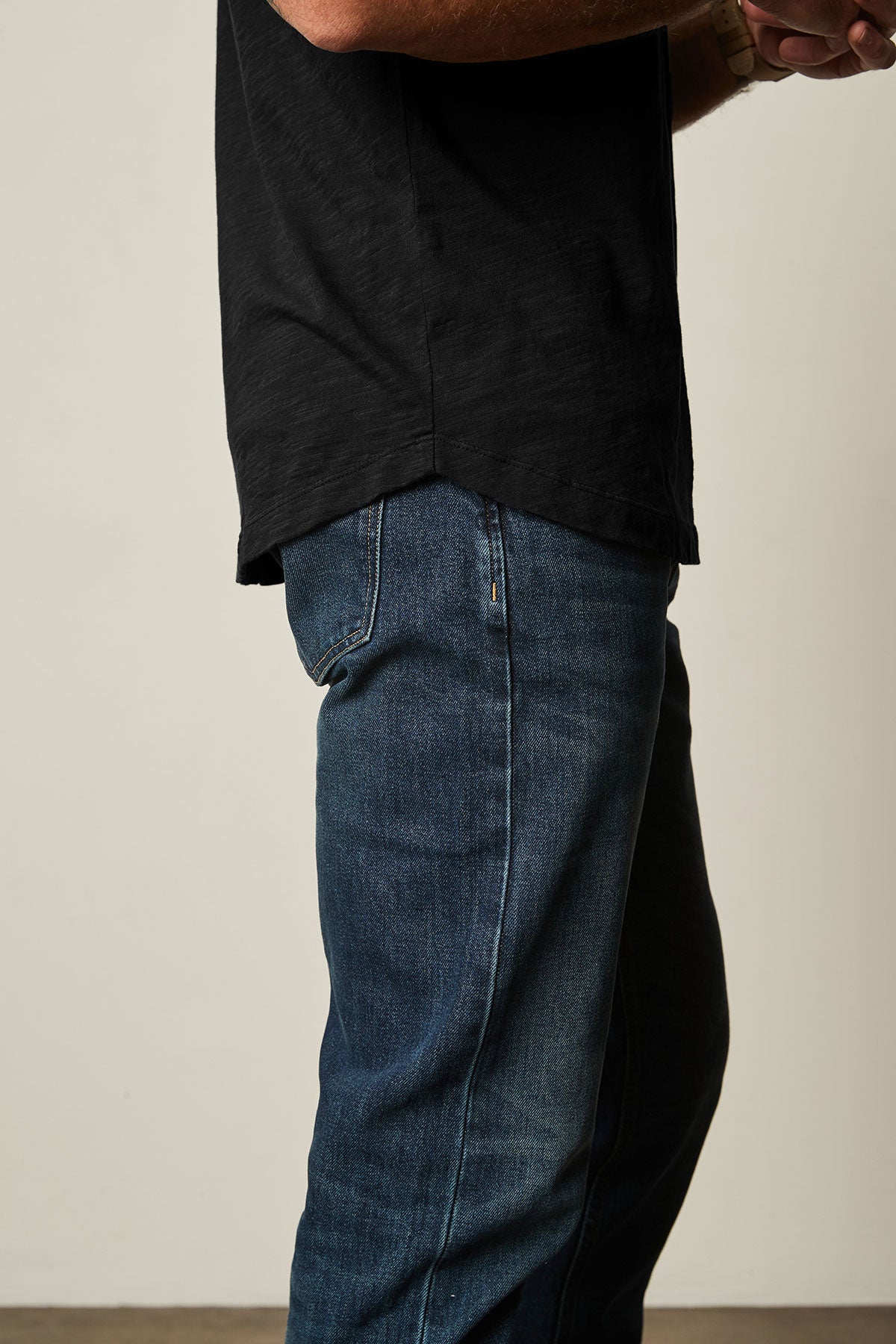 A person wearing an AMARO TEE by Velvet by Graham & Spencer in black, featuring a classic crew neckline and paired with blue jeans, stands sideways with crossed arms. The Peruvian cotton fabric makes the shirt perfect for layering in any season.-39026123440321