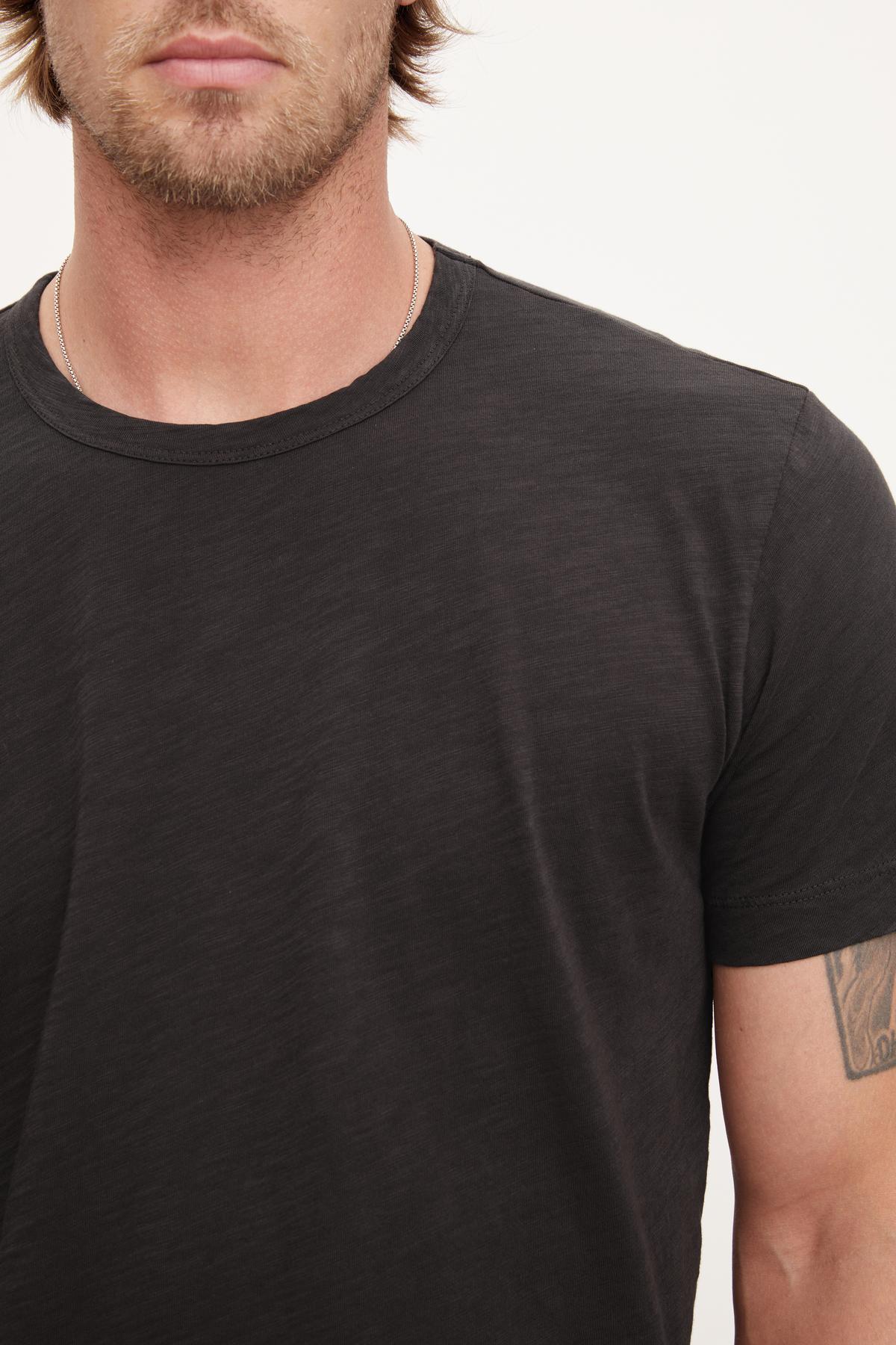   A man wearing a black crew neck Velvet by Graham & Spencer AMARO TEE with a visible tattoo on his left arm. 