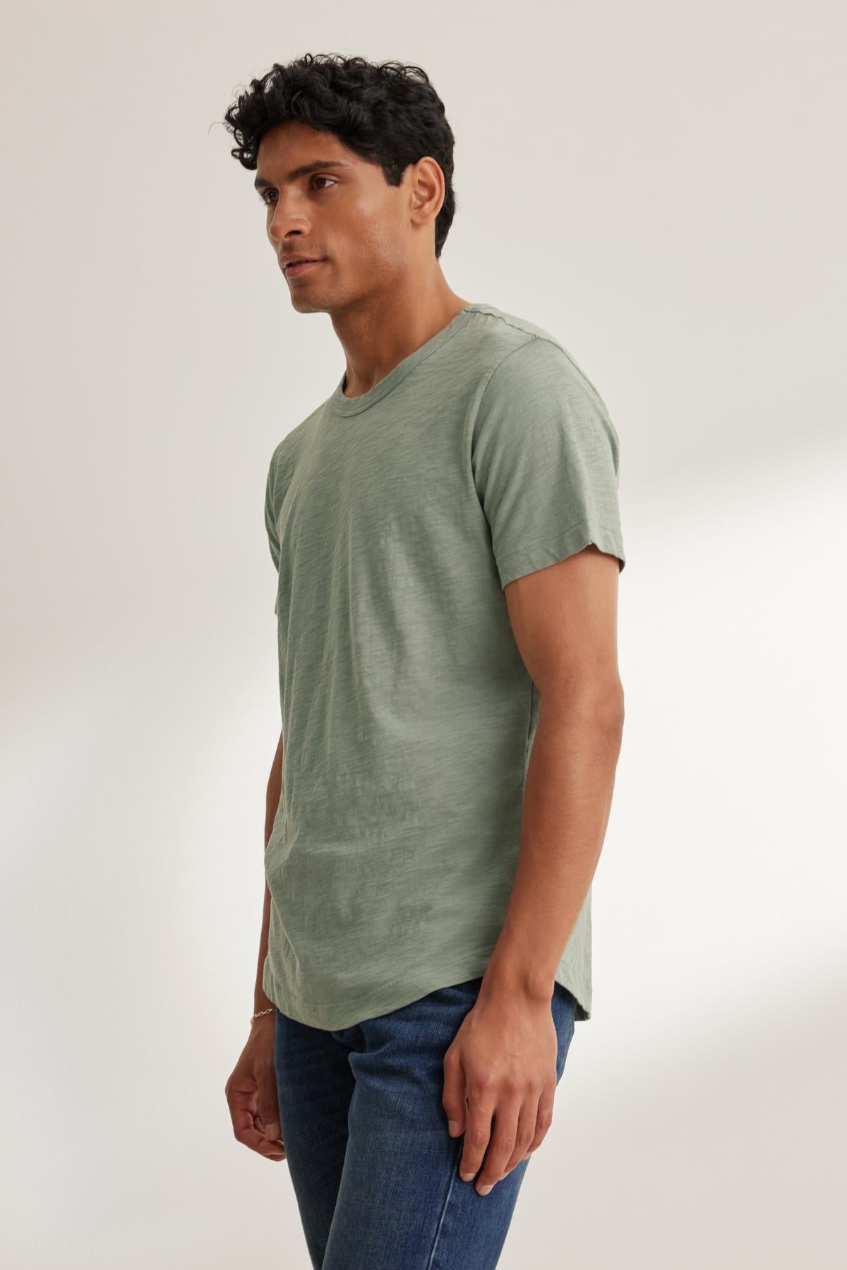   A person wearing a light green AMARO TEE by Velvet by Graham & Spencer, made of lightweight Peruvian cotton with a classic crew neckline, stands against a neutral background. 