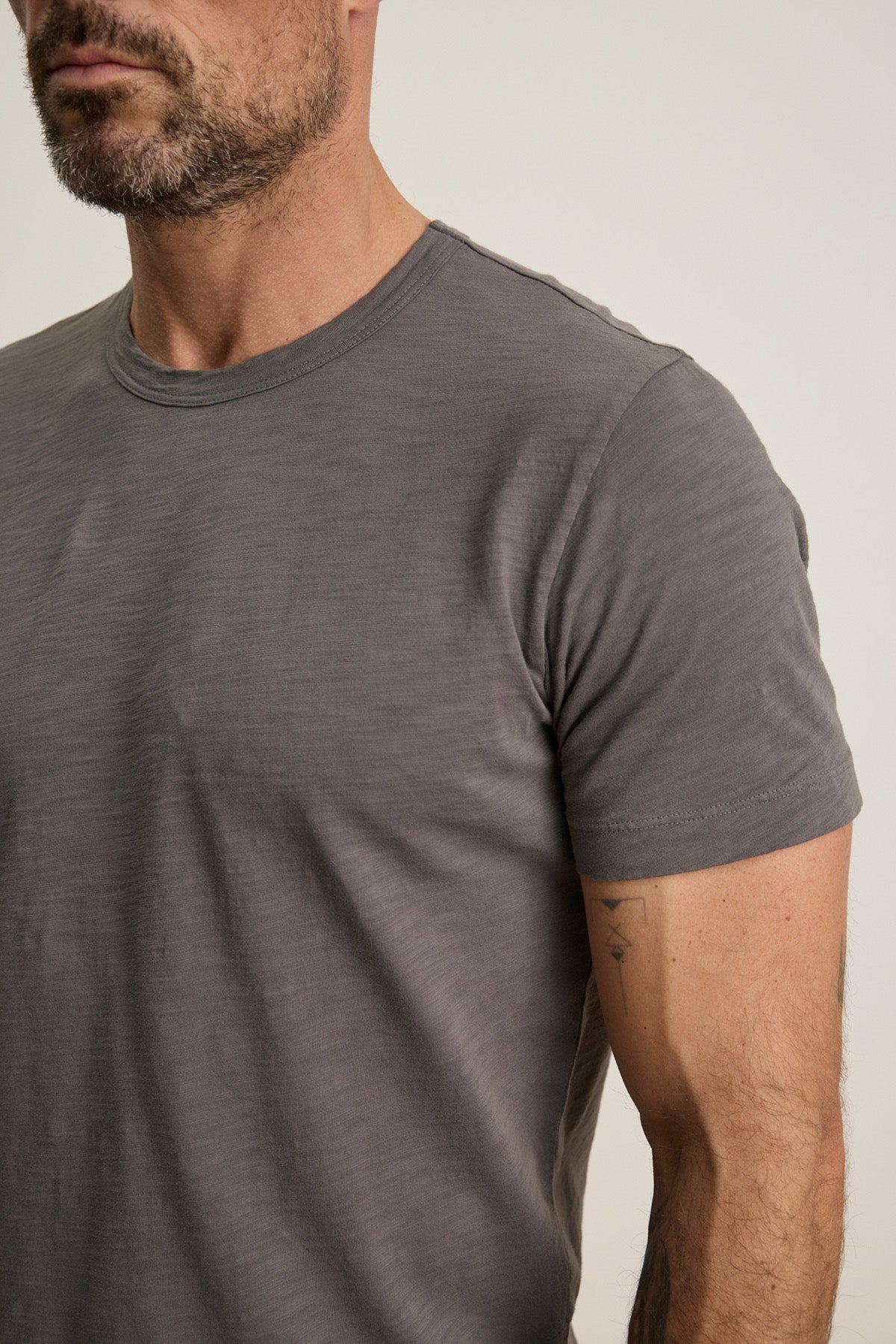 A man with short facial hair wears the AMARO TEE by Velvet by Graham & Spencer, a plain grey crew neck t-shirt crafted from soft Peruvian cotton, shown from the waist up against a neutral background.-40452464804033
