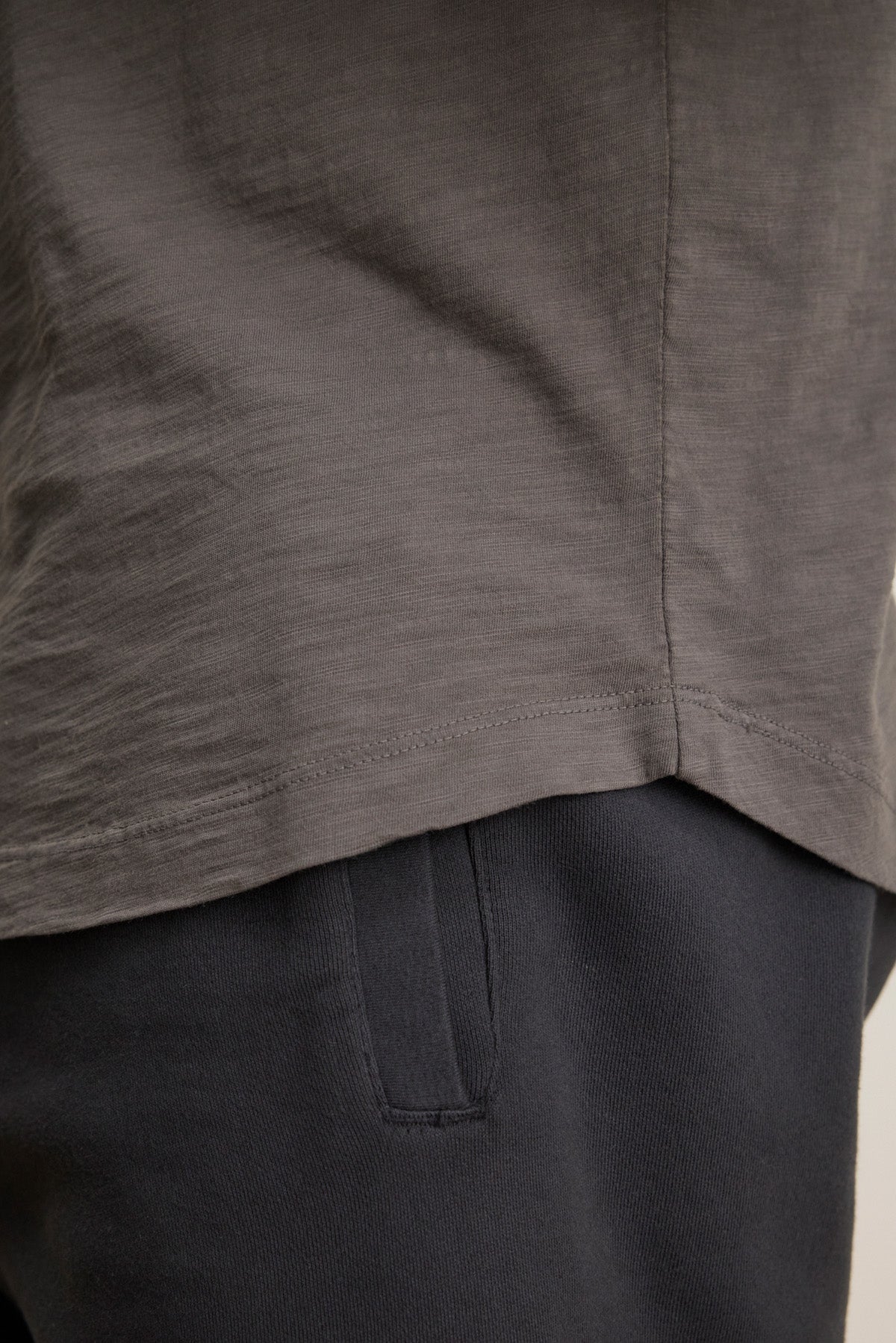 Close-up of a person wearing the AMARO TEE by Velvet by Graham & Spencer in grey Peruvian cotton and dark pants, highlighting the shirt's hem and pocketed waistband—perfect as a soft layering piece.