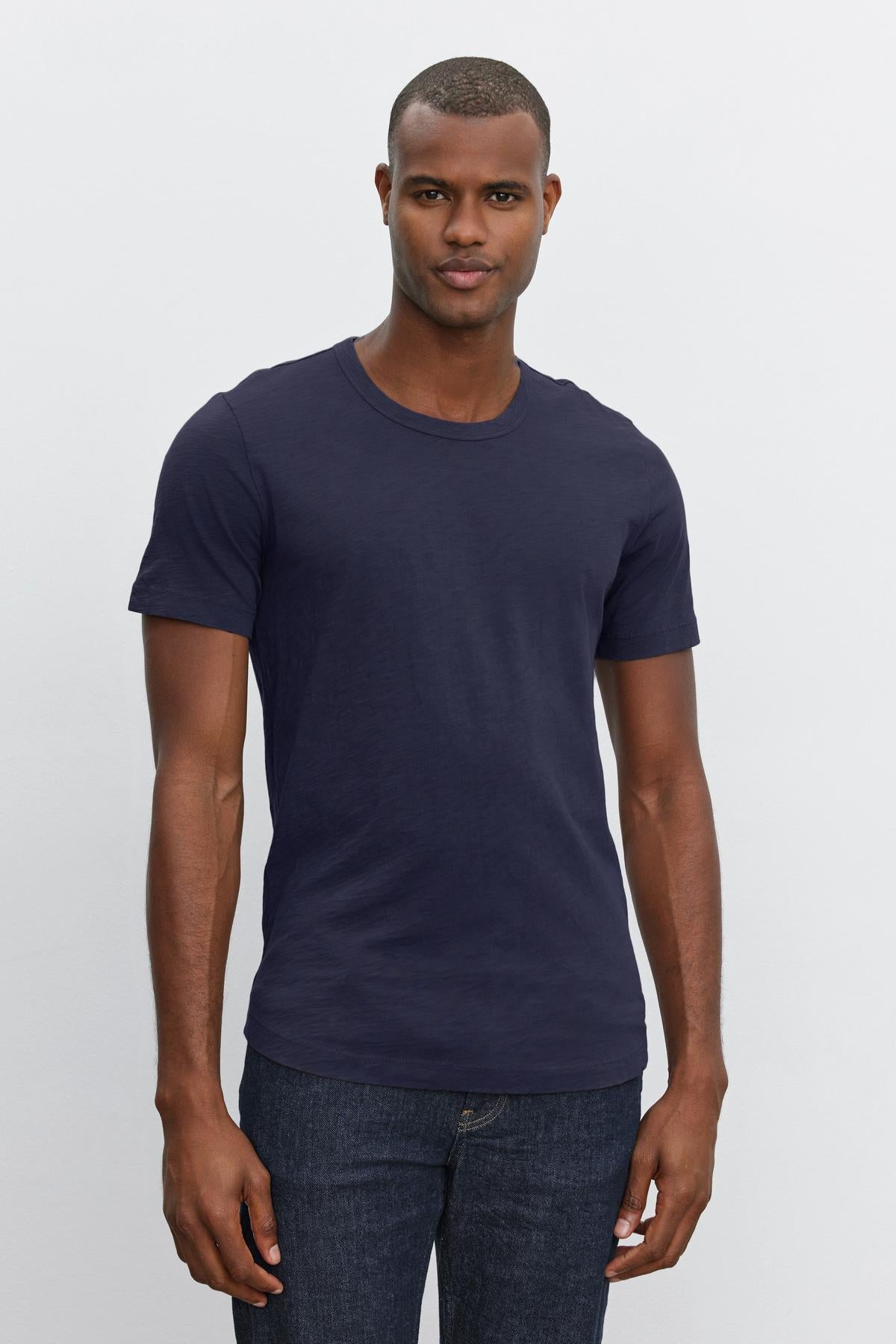 Man wearing a navy blue Velvet by Graham & Spencer AMARO TEE and jeans standing against a plain background.-36273921917121
