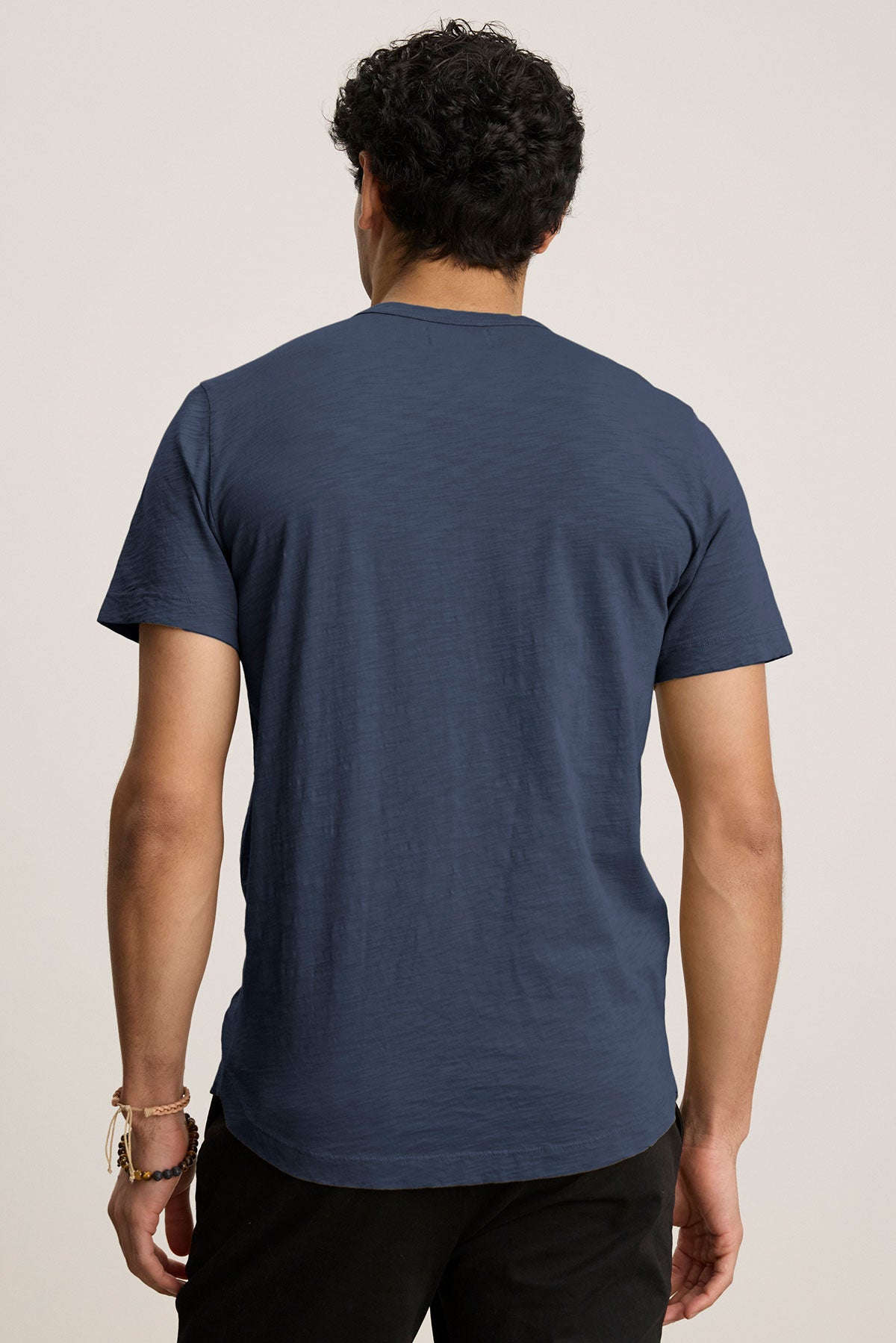   A person with their back to the camera wears a navy AMARO TEE crafted from soft Peruvian cotton by Velvet by Graham & Spencer, paired with black pants against a plain background. 