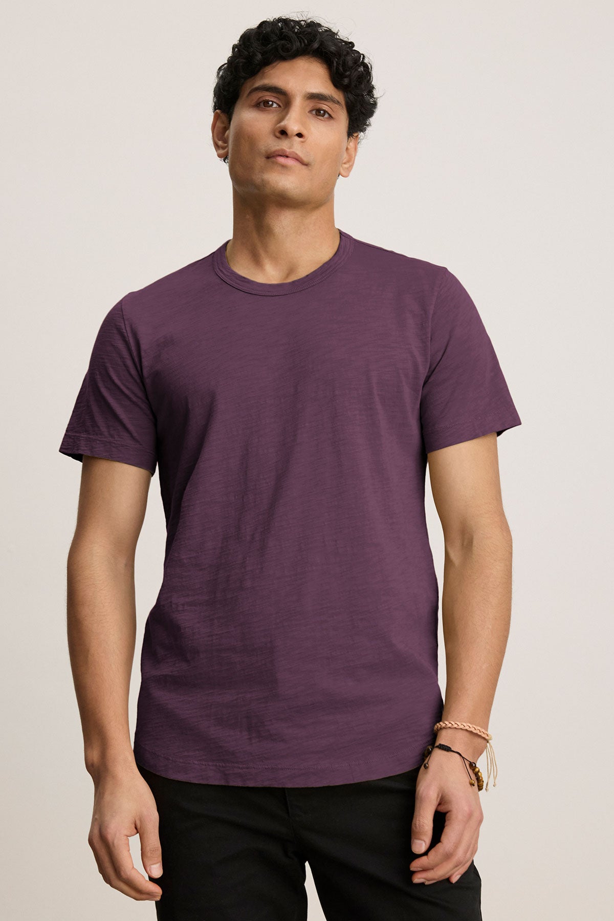   Against a plain background, a person wears Velvet by Graham & Spencer's AMARO TEE—crafted from lightweight Peruvian cotton with a classic crew neckline—and black pants, creating a polished yet casual look. 