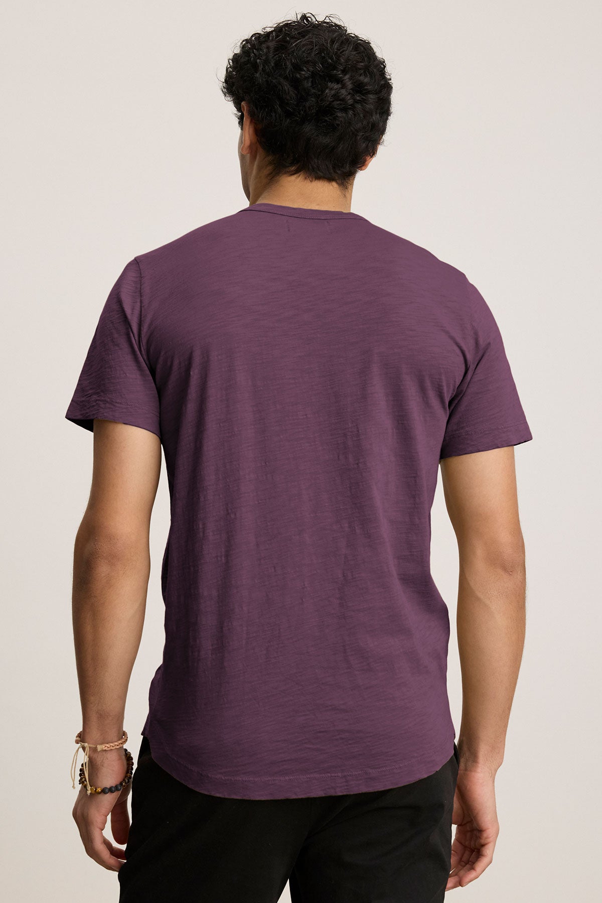   A person in a purple AMARO TEE by Velvet by Graham & Spencer, featuring a classic crew neckline, stands with their back to the camera. The lightweight Peruvian cotton makes it perfect for layering on any occasion. They are also wearing black pants. 