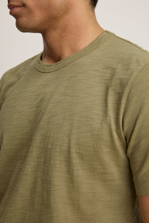 The AMARO TEE by Velvet by Graham & Spencer is a light olive green, short-sleeve crewneck made from soft Peruvian cotton, shown from shoulders to chin facing slightly left—an ideal layering piece for any outfit.