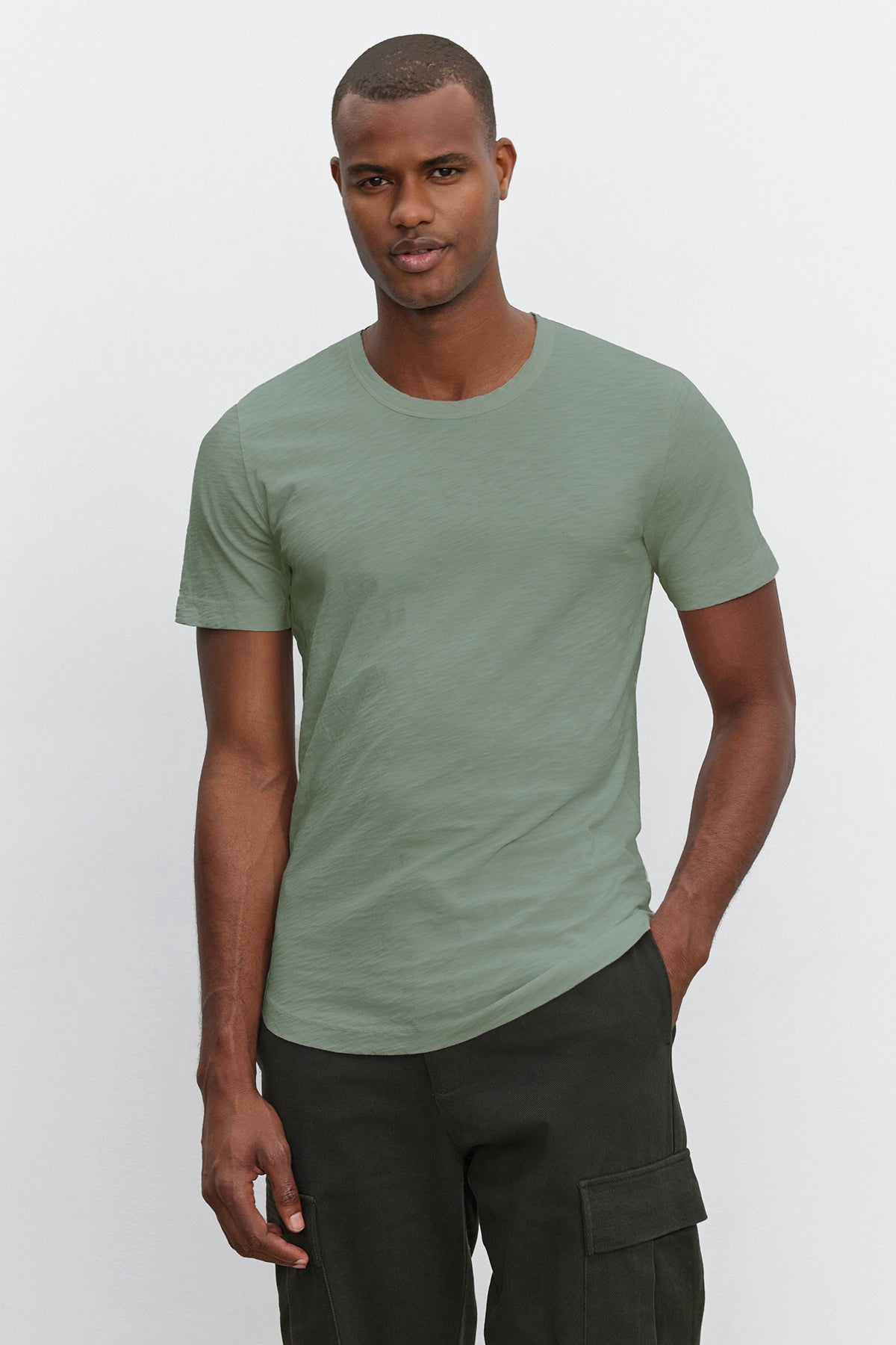 A man wearing a stylish light green AMARO TEE by Velvet by Graham & Spencer and black cargo pants stands against a plain white background.-36909384696001