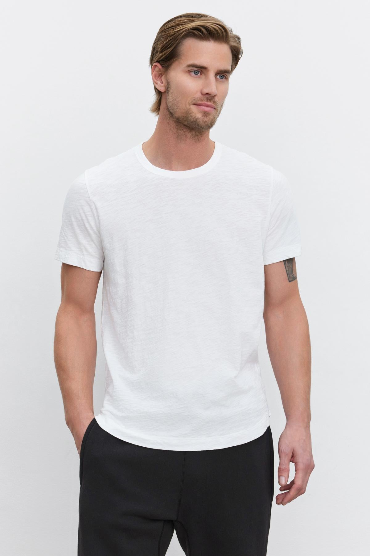 A man with blond hair posing in a white Velvet by Graham & Spencer slub knit AMARO TEE with a crew neck and black pants.-35867457519809