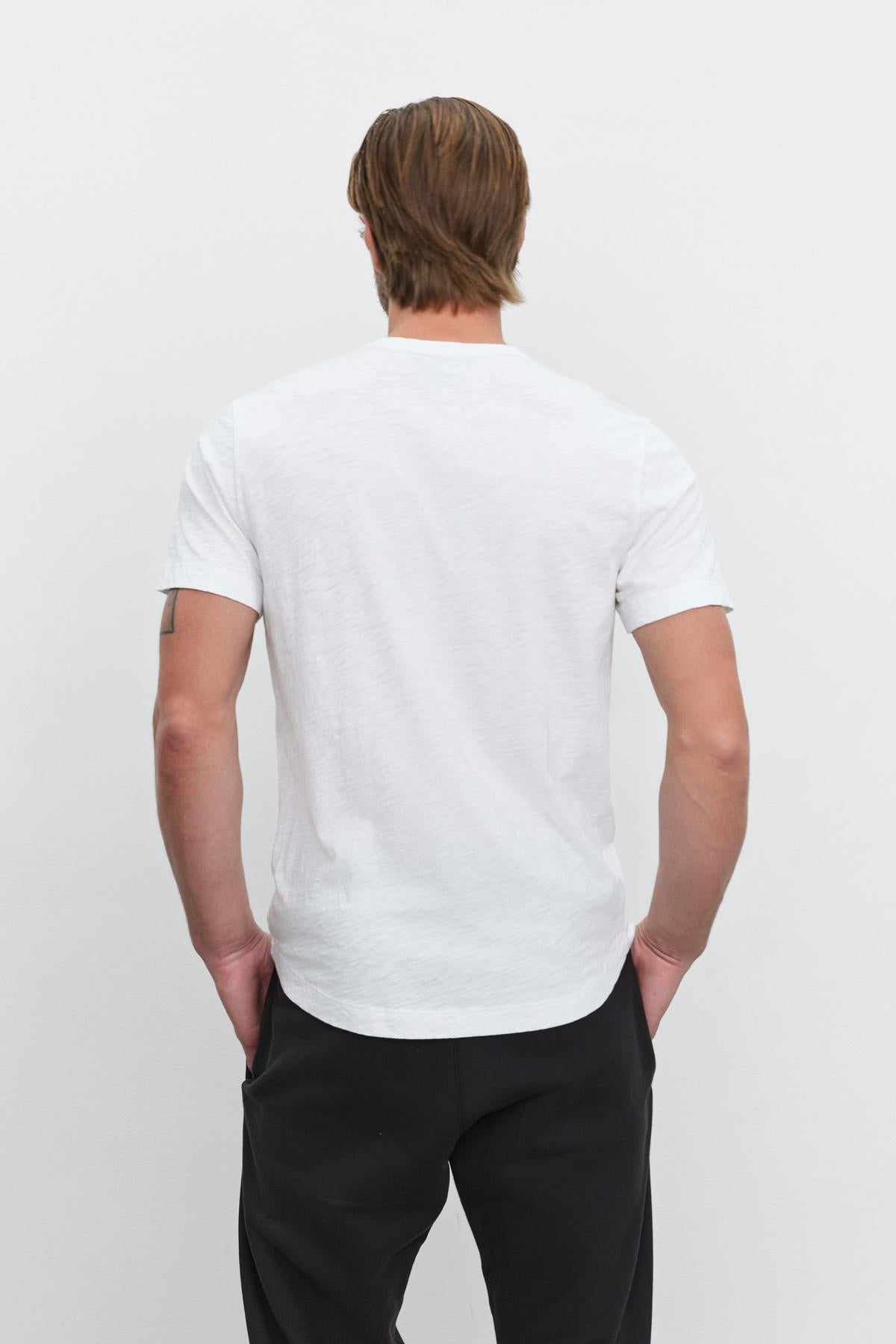 The back of a man wearing a Velvet by Graham & Spencer AMARO CREW NECK SLUB TEE with a curved hemline and black pants.-35867457585345