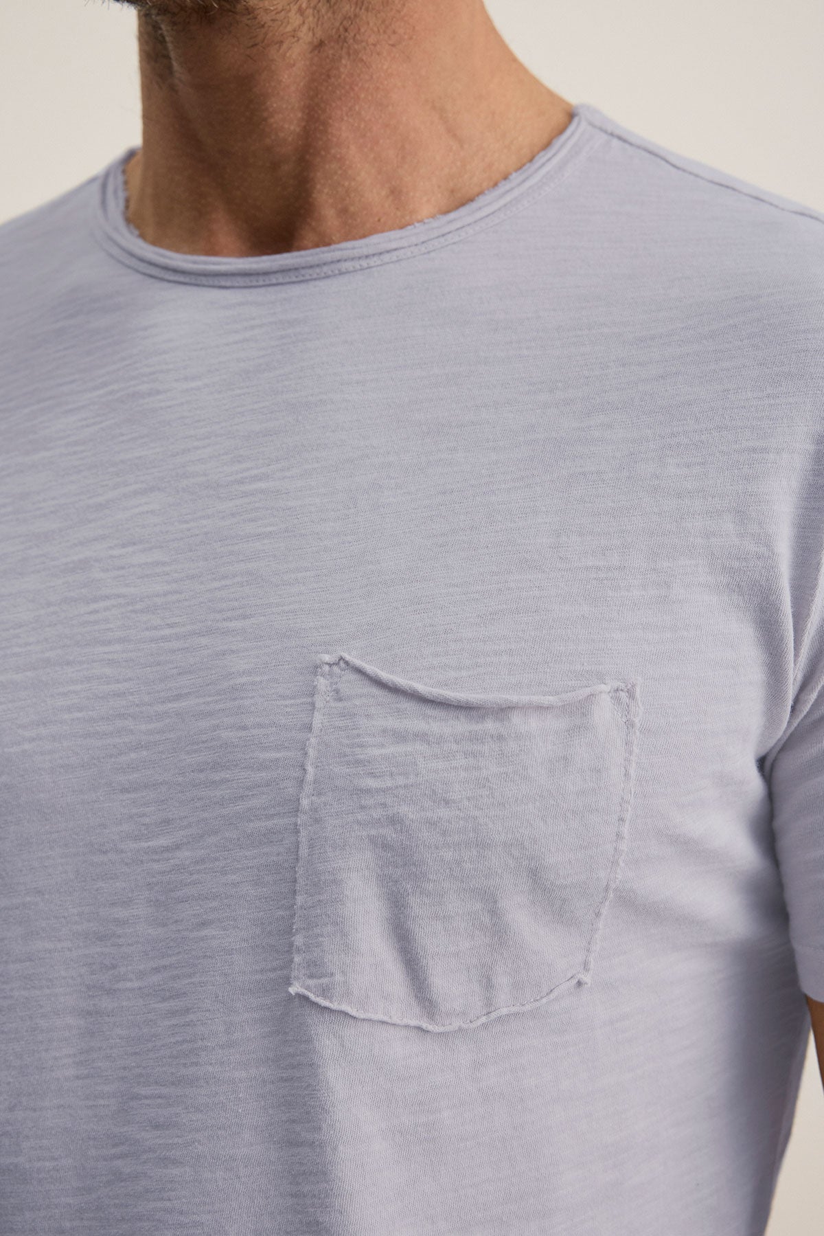   A person wearing the CHAD TEE by Velvet by Graham & Spencer, a light gray t-shirt made from soft Peruvian cotton, with a crew neckline and a small chest pocket. 
