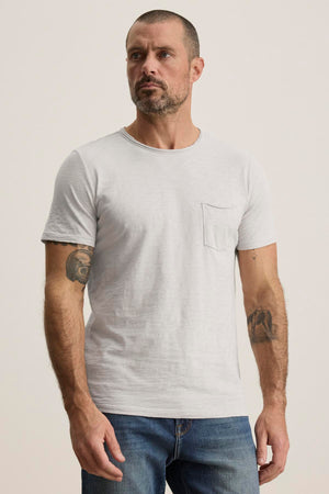 A man with short hair and a beard is wearing the CHAD TEE by Velvet by Graham & Spencer, showcasing his rugged style with tattoos on his arms.